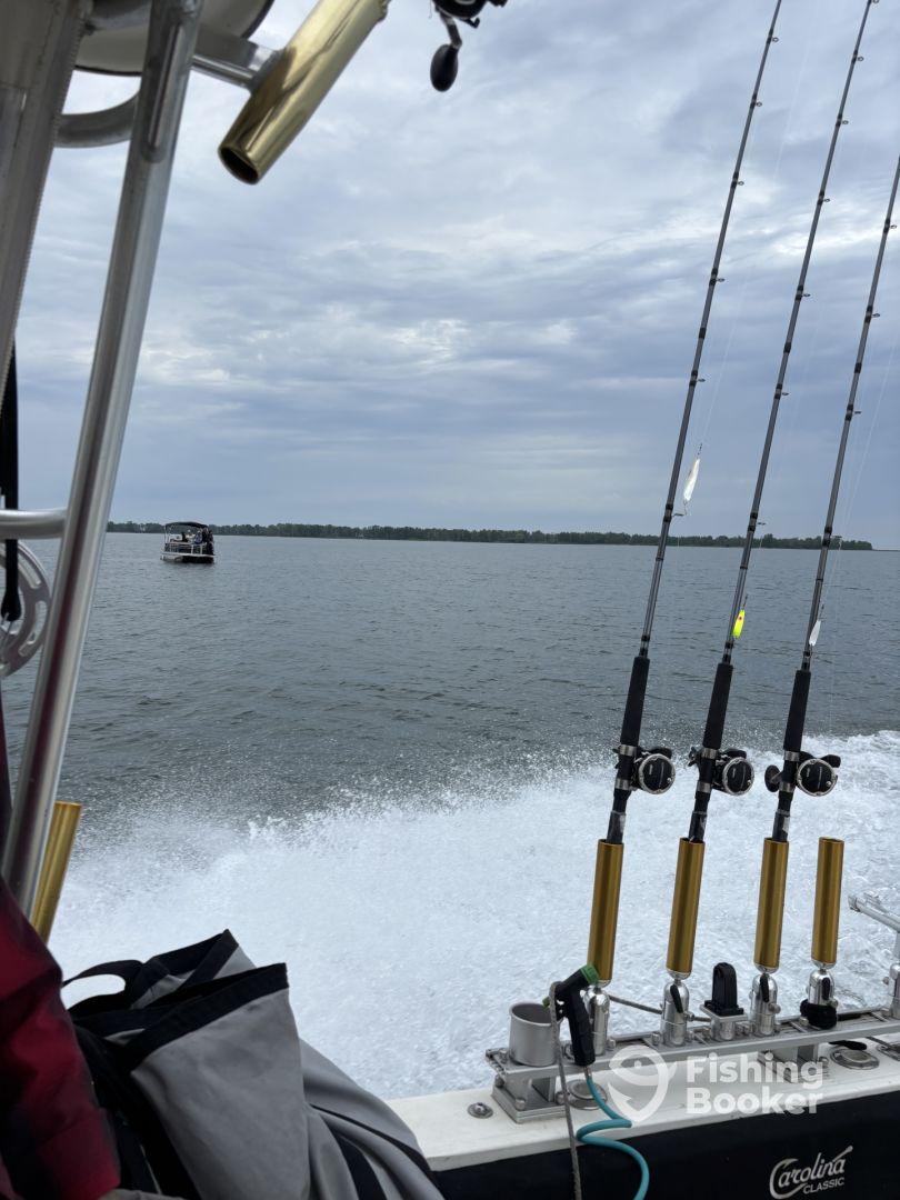 View from the interior of a Carolina Classic boat, showcasing fishing rods and the wake created while cruising on a calm waterway.