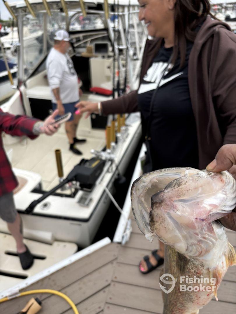 An angler proudly displaying a freshly caught fish while others are preparing on the boat in the background.