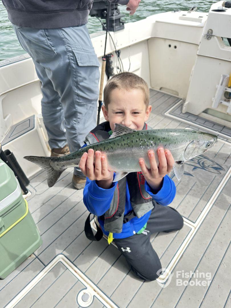 A young angler proudly displaying a caught fish while kneeling on the deck of a fishing boat.