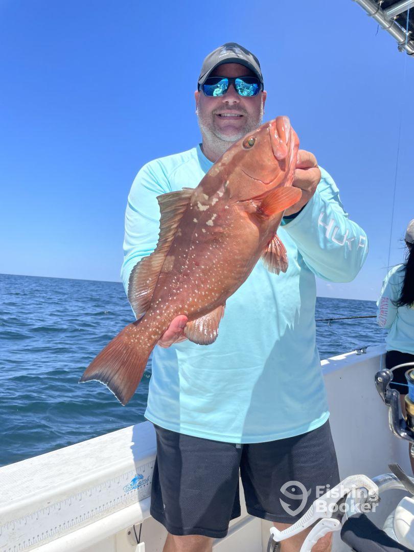 An angler proudly displaying a large Grouper while fishing offshore, showcasing a sunny day on the water.