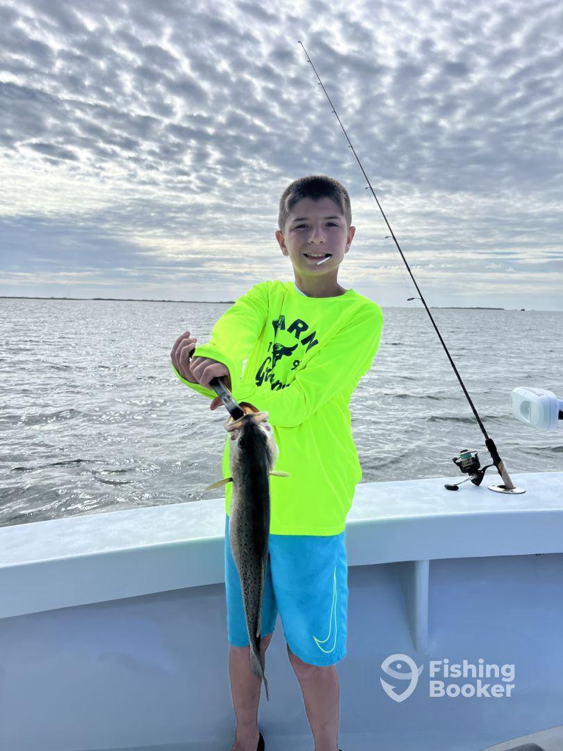 Young angler proudly holding a large fish while fishing on a boat, showcasing a successful catch in a scenic waterway.