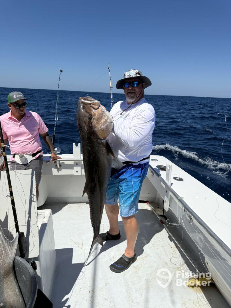 An angler proudly displays a large Grouper while fishing on a charter boat in open waters.
