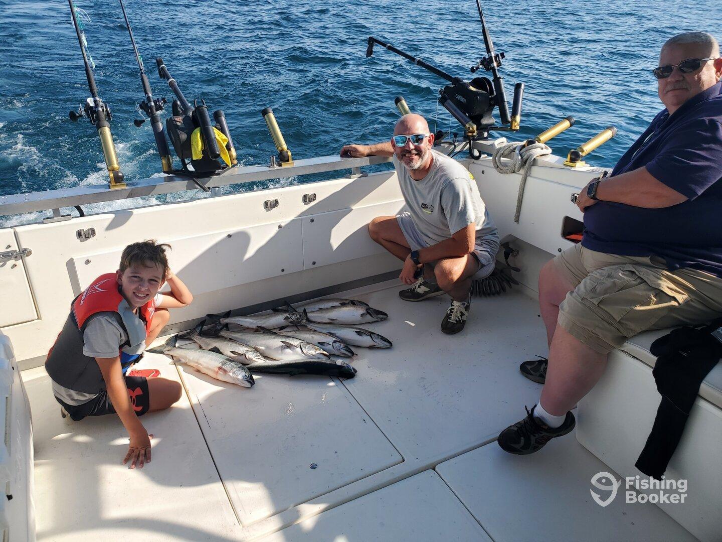 A young angler and two adults enjoying a successful fishing trip on a boat, showcasing a variety of fish on the deck.