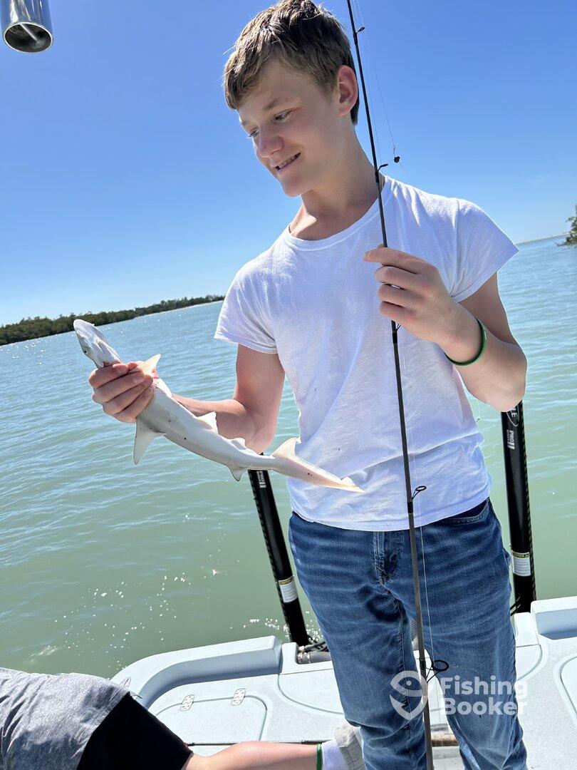 A young angler proudly holding a small shark while fishing on a sunny day.