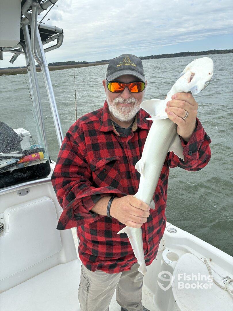 An angler proudly displaying a caught shark while on a fishing trip in a coastal waterway.