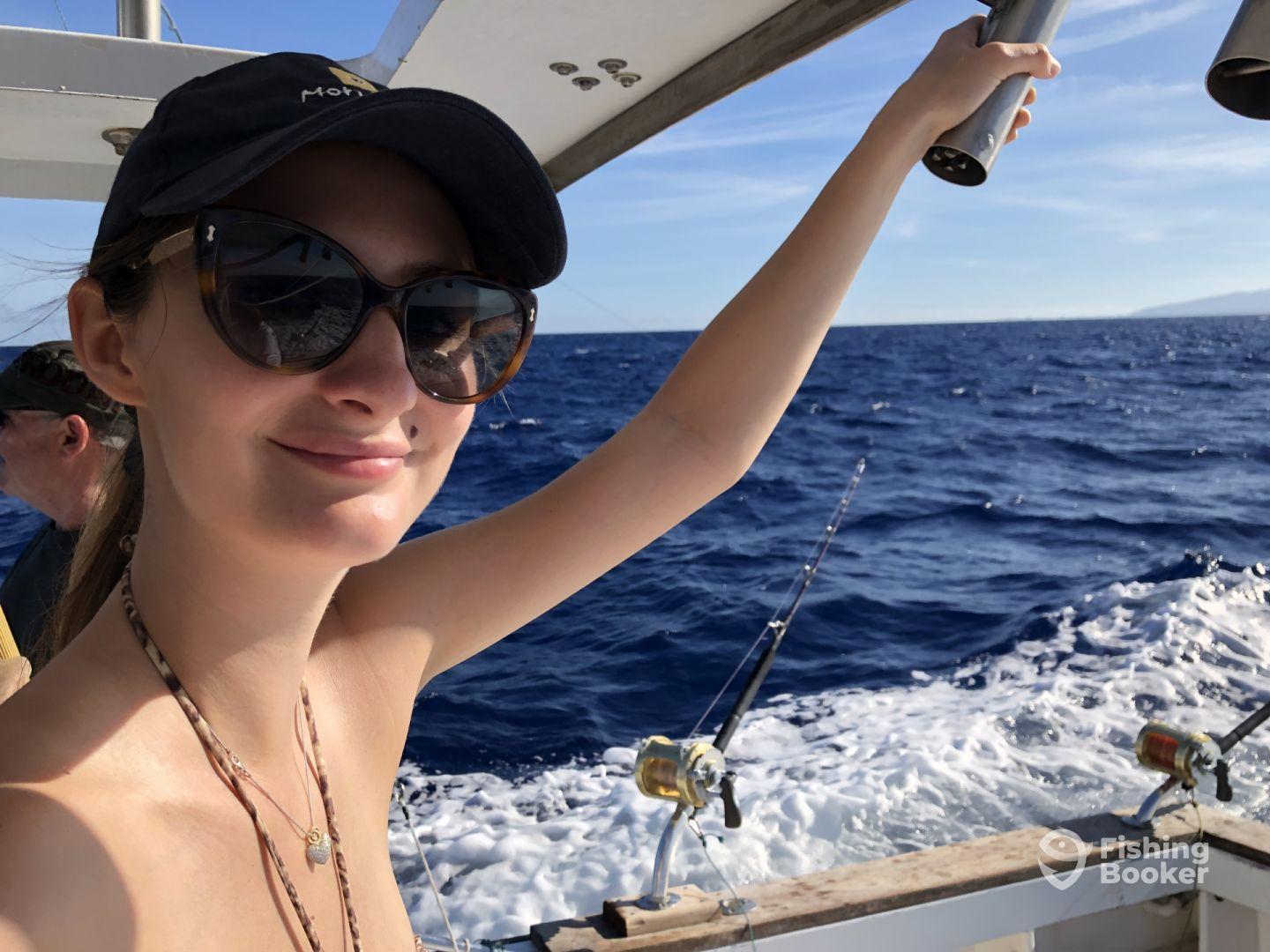 A young woman enjoying a sunny day on a fishing boat, with the ocean in the background, showcasing a relaxed fishing atmosphere.
