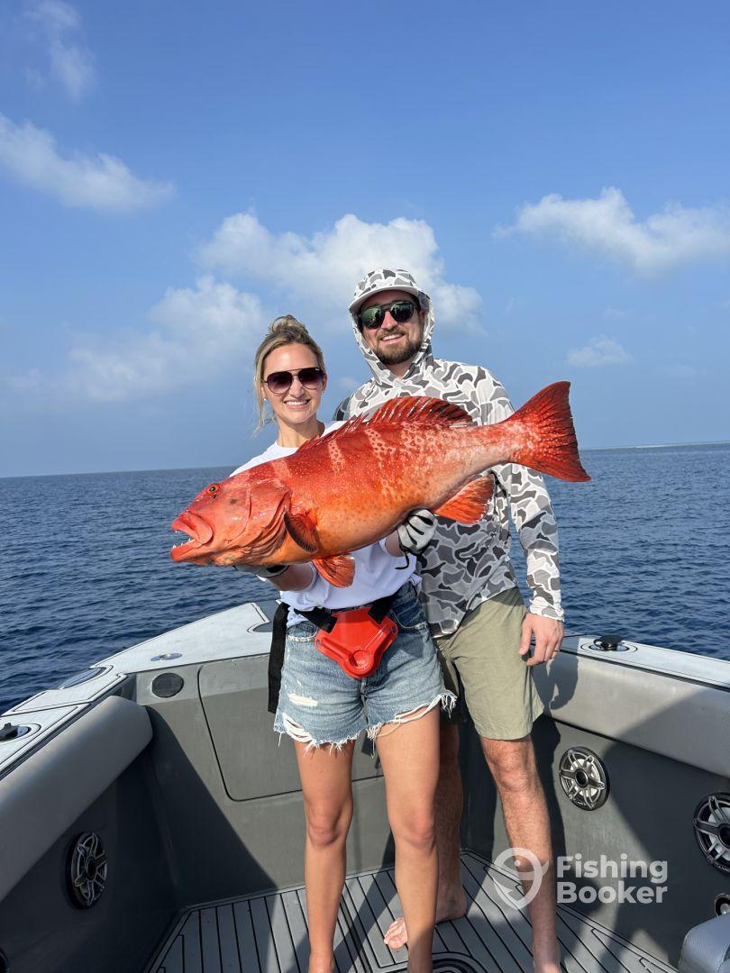 Two anglers proudly displaying a large Red Snapper on a boat during a deep-sea fishing trip.