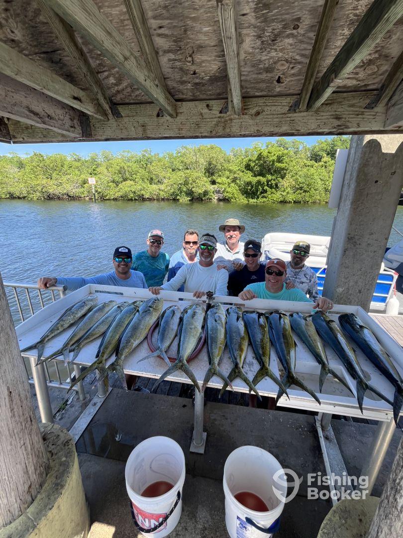 A group of anglers proudly displaying a catch of Mahi Mahi on a cleaning table at a dock, showcasing a successful fishing trip.