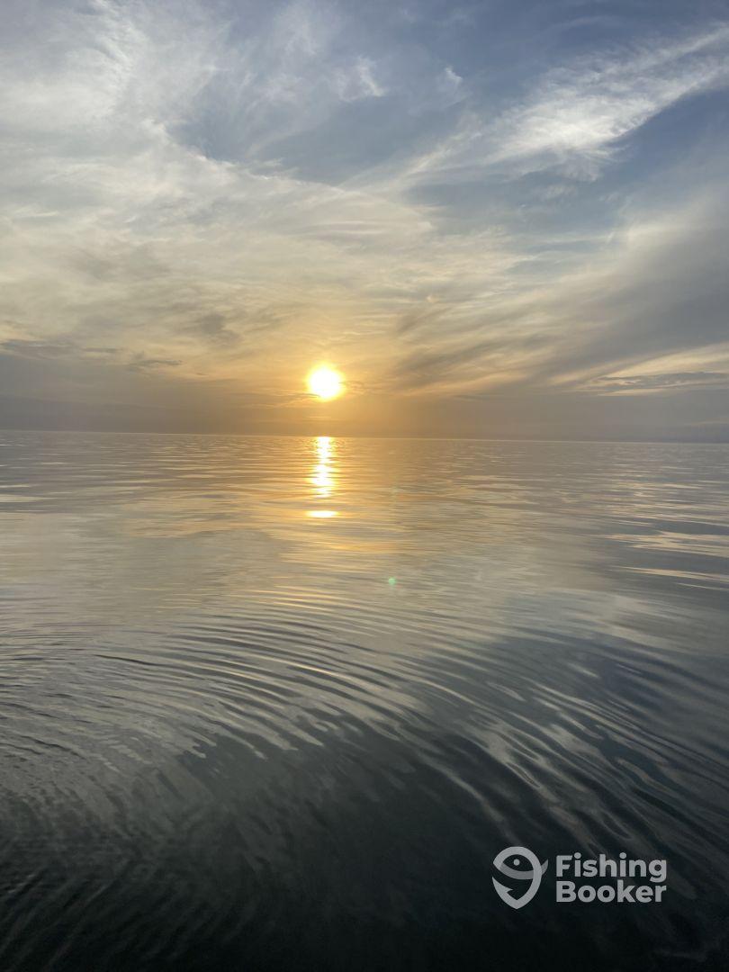 A serene sunset over calm waters, reflecting warm hues, creating a tranquil fishing environment.