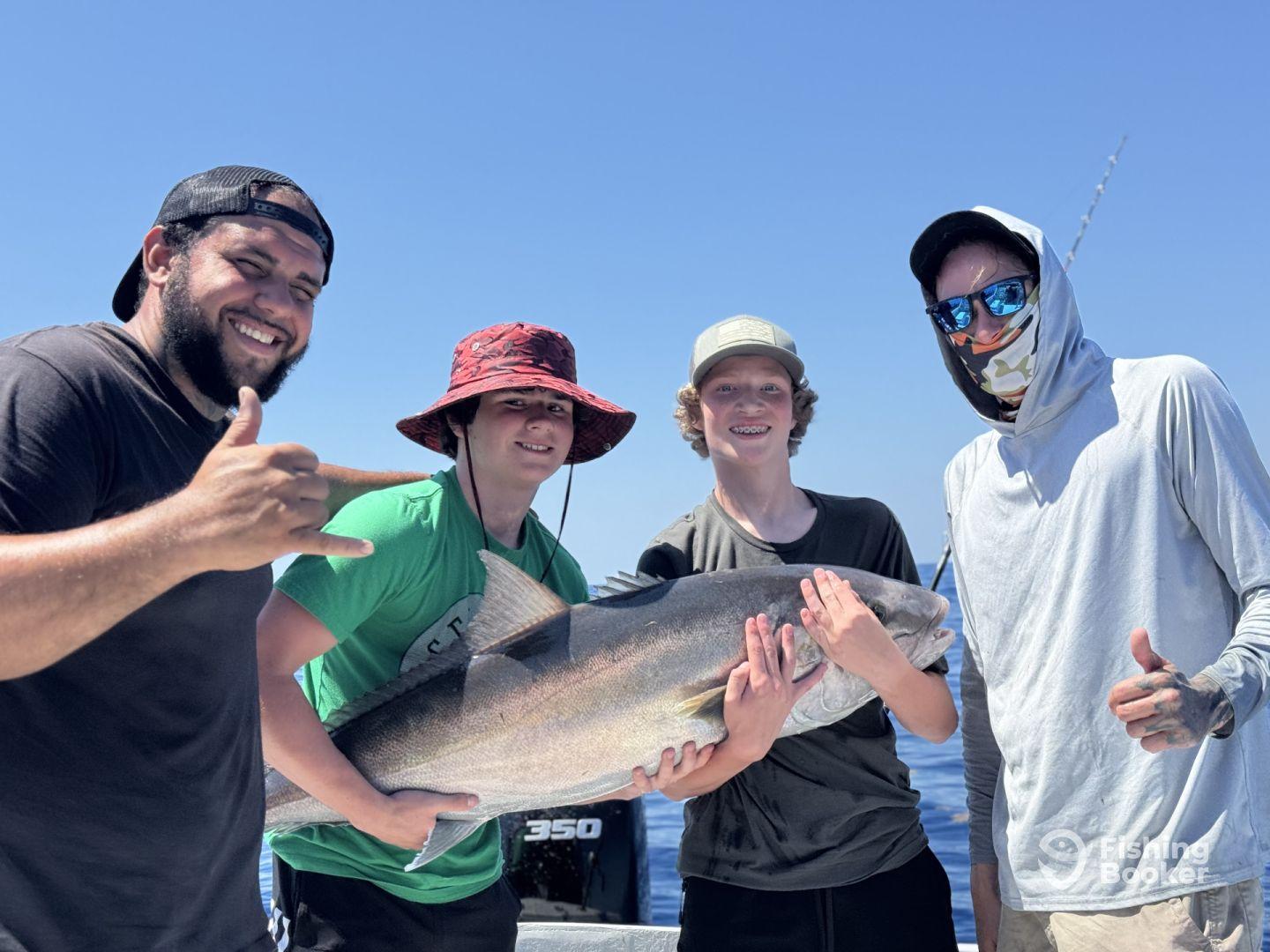 A group of young anglers proudly displaying a large fish on a sunny day at sea, showcasing their successful catch during a fishing charter.